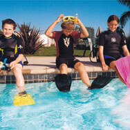 Kids wearing flippers and sitting on edge of pool